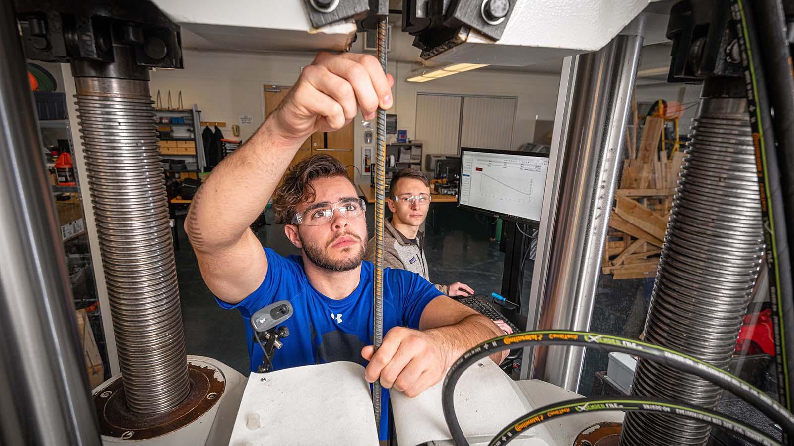 Two construction management students in shop cutting rebar